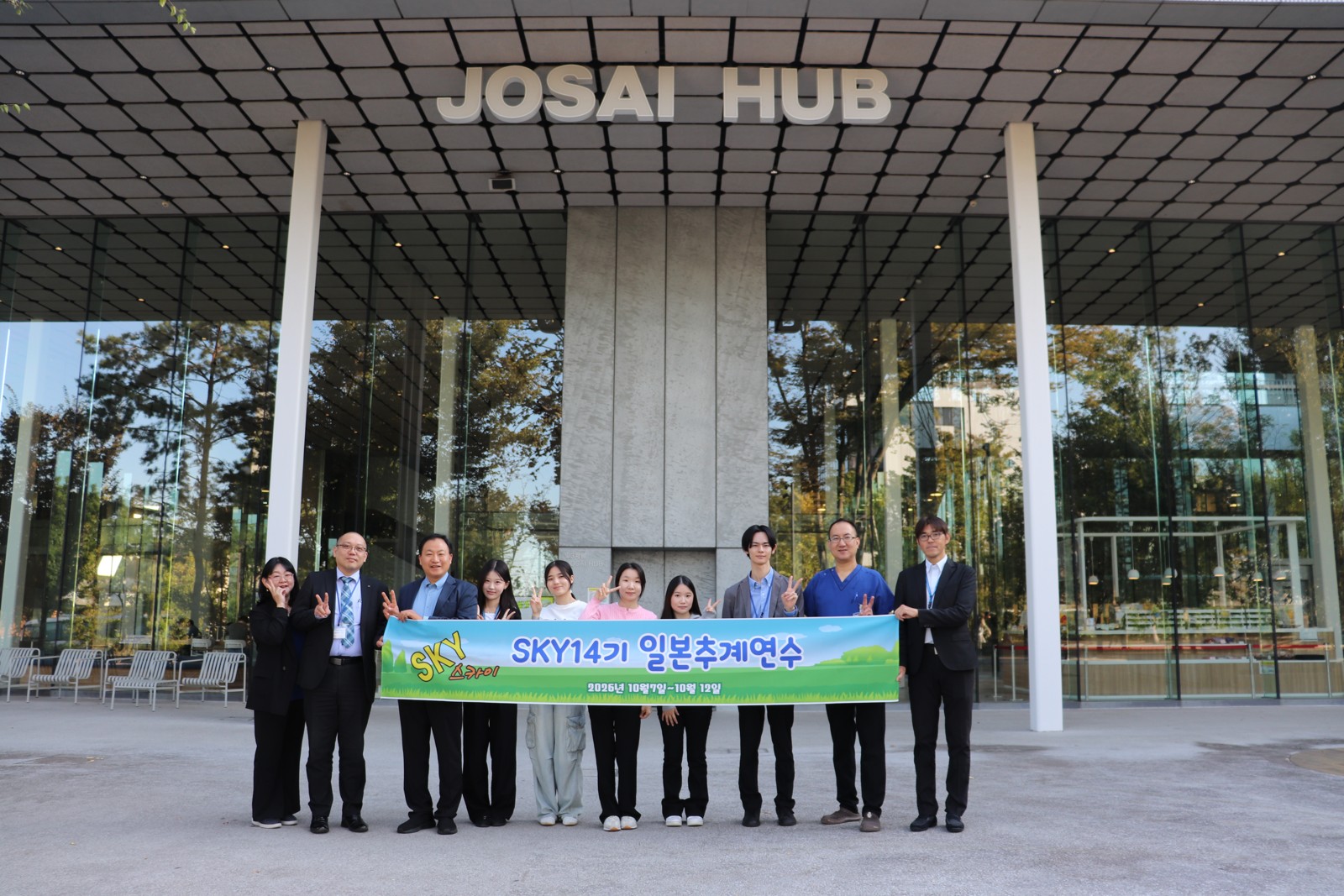 JOSAI HUBの入口前で横断幕を持つ訪問者と関係者